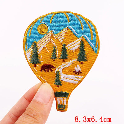 Embroidered patch of a hot air balloon with a mountain and camping scene held by a hand.