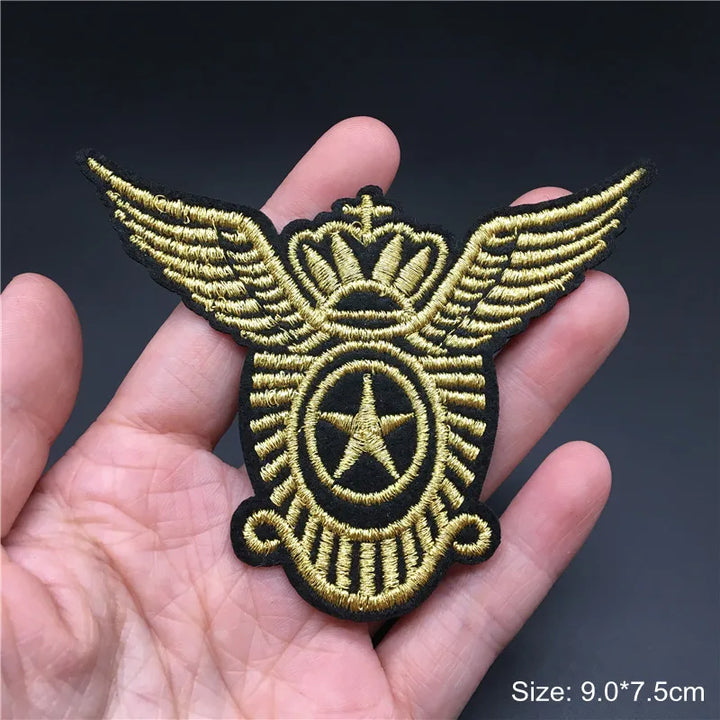 Gold and black embroidered patch with wings and star held in a hand against a dark background