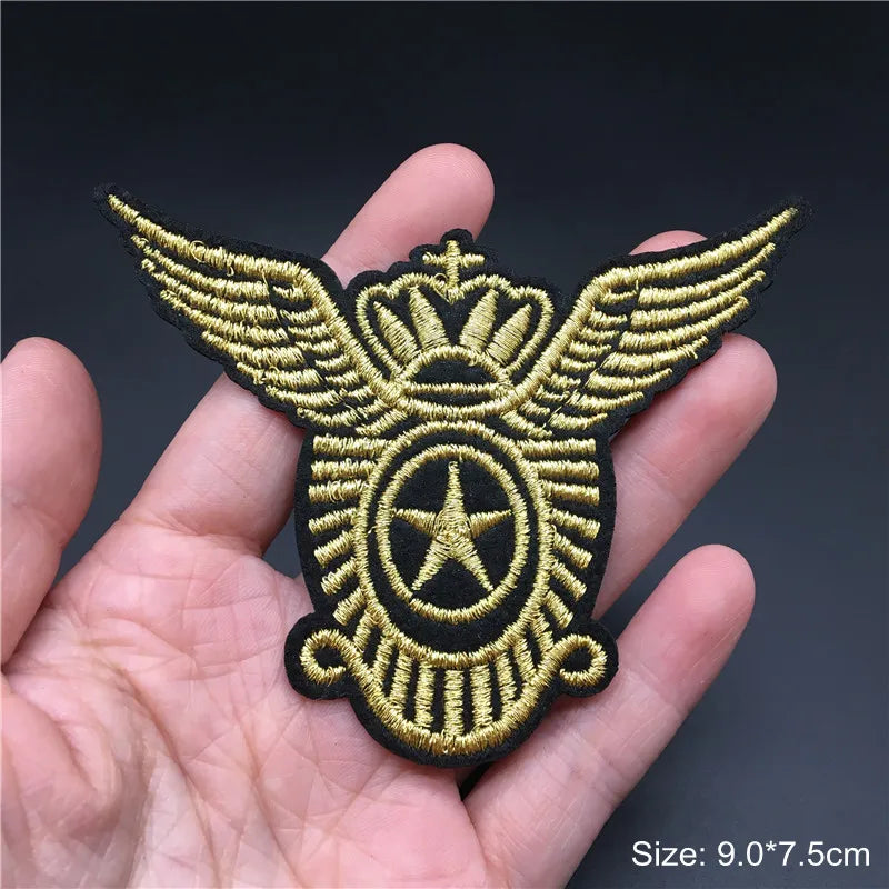 Gold and black embroidered patch with wings and star held in a hand against a dark background