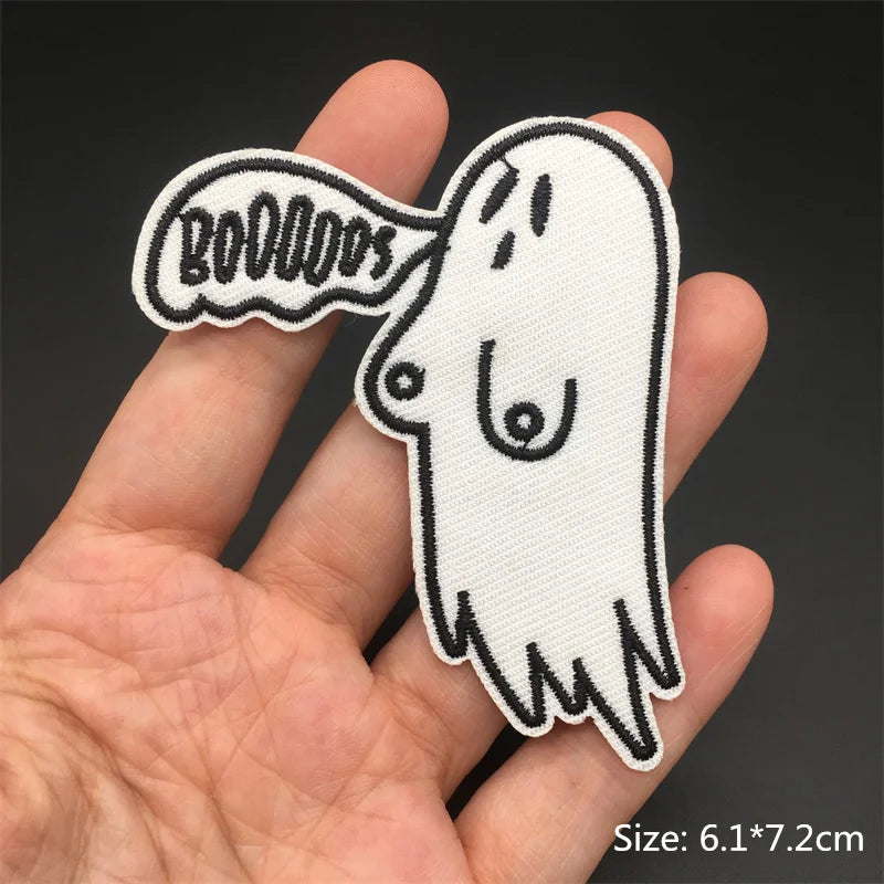 Ghost-shaped patch with 'BOO' text held in a hand against a dark background