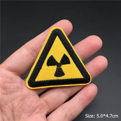 Yellow and black radiation warning patch held in a hand with a dark background