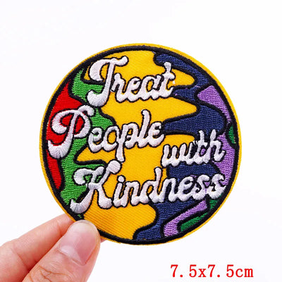 Round patch with 'Treat People with Kindness' text in colorful border held by a hand.