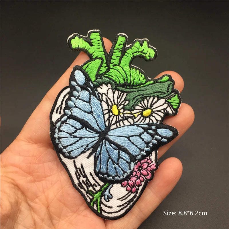 Embroidered patch with a butterfly and floral design held in a hand against a dark background.