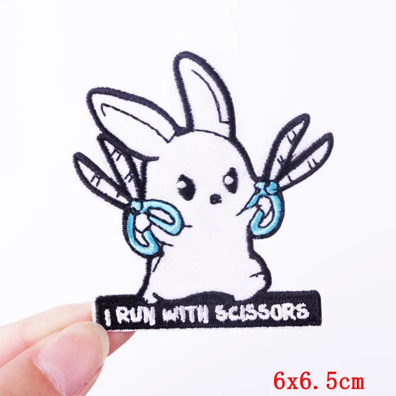Embroidered patch of a rabbit holding scissors with text 'I Run with Scissors' held by a hand on a white background.