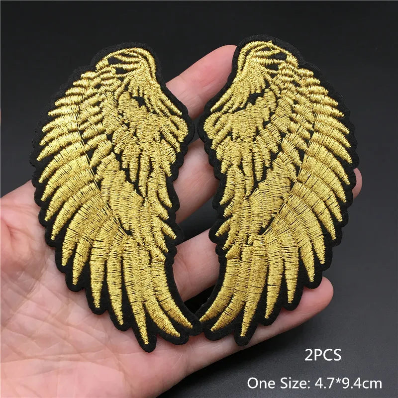 Gold angel wings patch held in a hand with a dark background