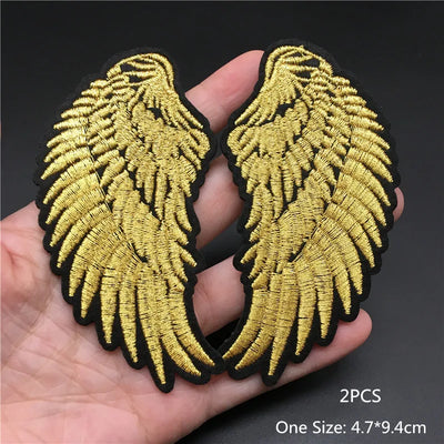 Gold angel wings patch held in a hand with a dark background