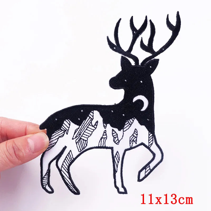 Black silhouette of a deer with mountains on a white background, held by a hand.