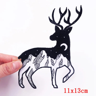 Black silhouette of a deer with mountains on a white background, held by a hand.