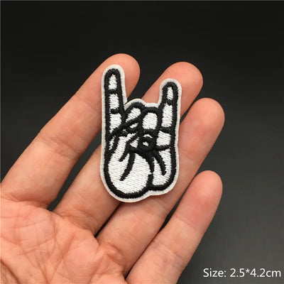 Hand holding a black and white embroidered patch of a hand making a peace sign with a rock-on symbol.