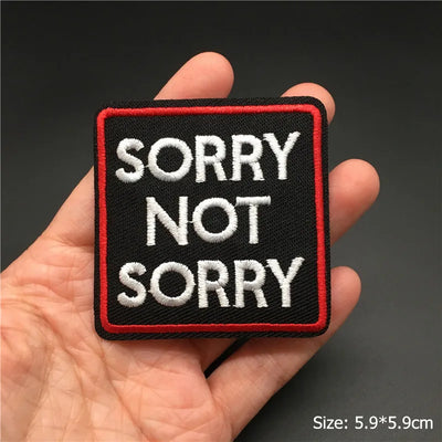 Embroidered patch with 'SORRY NOT SORRY' text held in a hand against a dark background