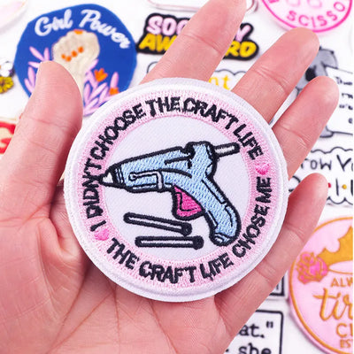 Patch with text and a hot glue gun illustration held in a hand, surrounded by other patches.