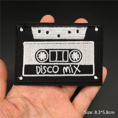 Embroidered patch of a cassette tape labeled 'Disco Mix' held in a hand against a dark background.