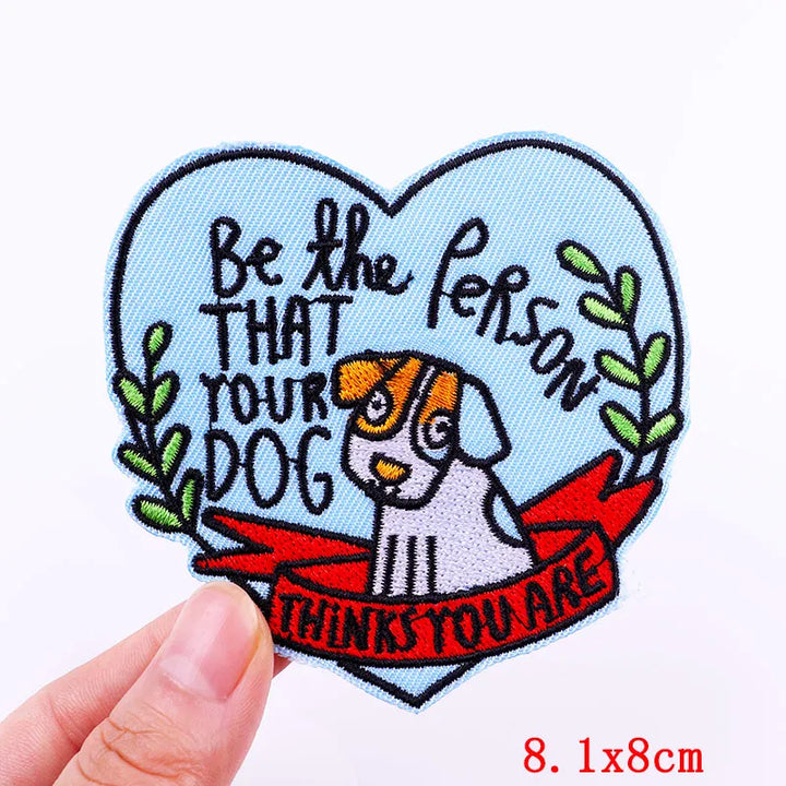 Heart-shaped patch with a dog illustration and text held by a hand on a white background