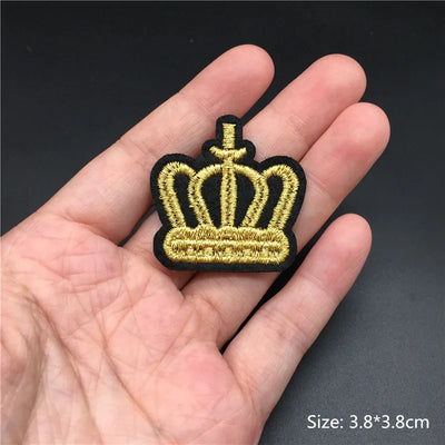 Gold and black crown patch held in a hand with a dark background