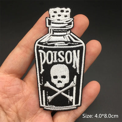 Embroidered patch of a poison bottle with skull and crossbones design held in a hand.