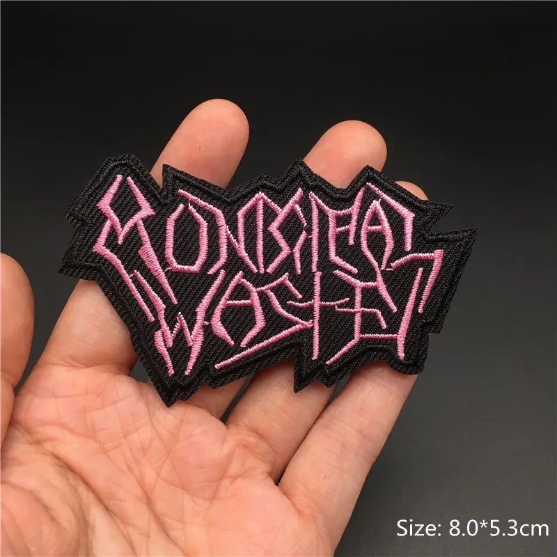 Black patch with pink text held in a hand against a dark background