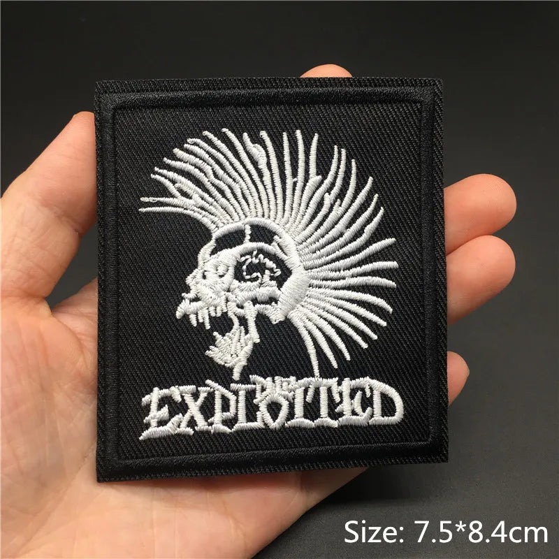 Embroidered patch with a lion design and 'The Exploited' text held in a hand against a dark background.