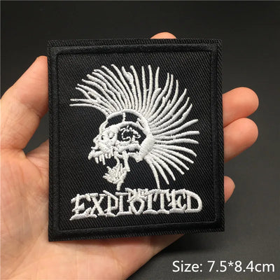 Embroidered patch with a lion design and 'The Exploited' text held in a hand against a dark background.