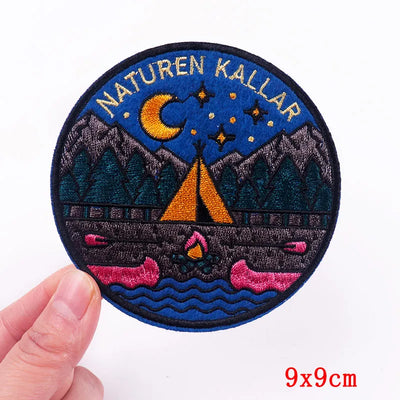 Embroidered patch with mountains, tent, and crocodile design held by a hand on a white background.
