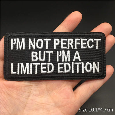 Black patch with white text held in a hand against a dark background