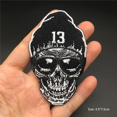 Skull patch with number 13 held in a hand against a dark background