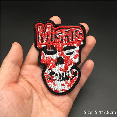 Embroidered patch with a skull design and 'Misfits' text held in a hand against a dark background.