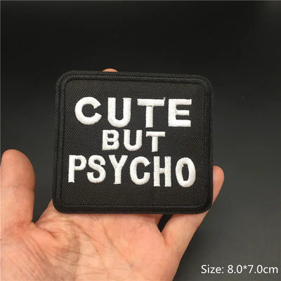Black patch with 'Cute But Psycho' text held in a hand against a dark background
