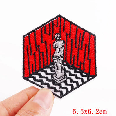 Hexagonal patch with red text and a statue design held by a hand, on a white background.