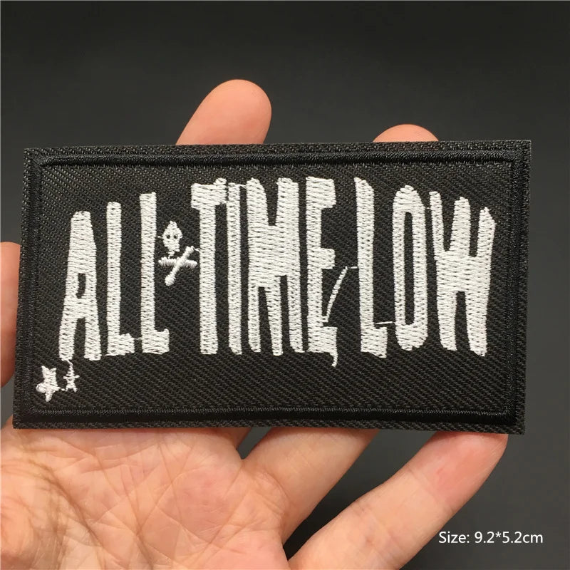 Embroidered patch with 'All Time Low' text held in a hand against a dark background