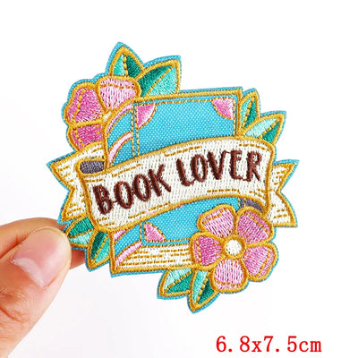 Embroidered patch with 'BOOK LOVER' text held by a hand, on a white background.