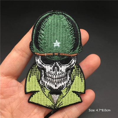 Embroidered patch of a skull wearing a green military uniform held in a hand.