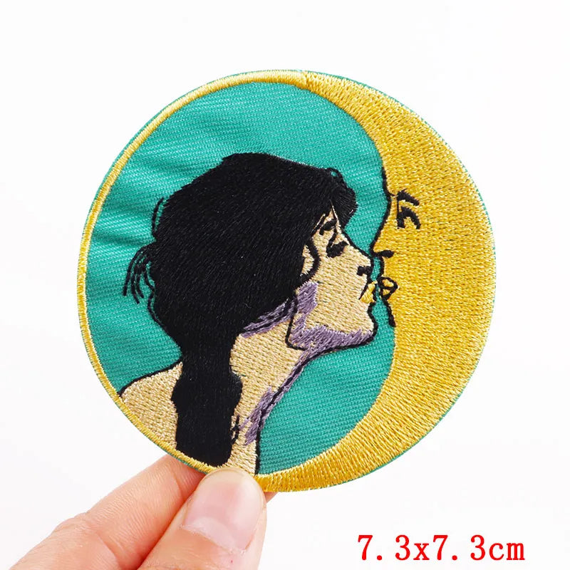 Circular patch with embroidered design of a profiled face held by a hand on a white background.