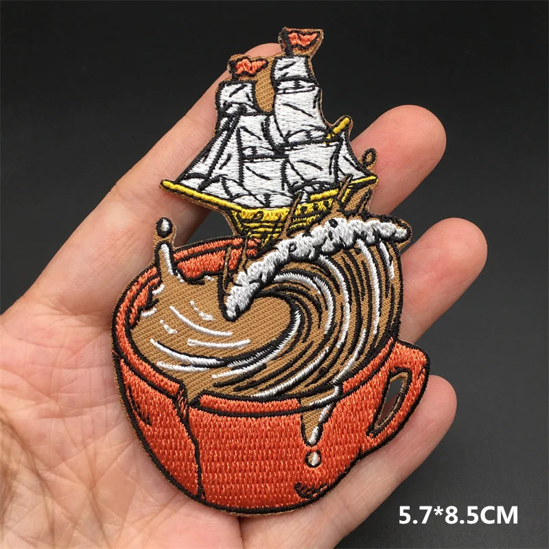 Embroidered patch of a ship on a wave held in a hand with a dark background