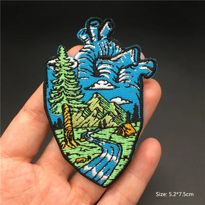 Hand holding a embroidered patch with a mountain and nature design against a dark background