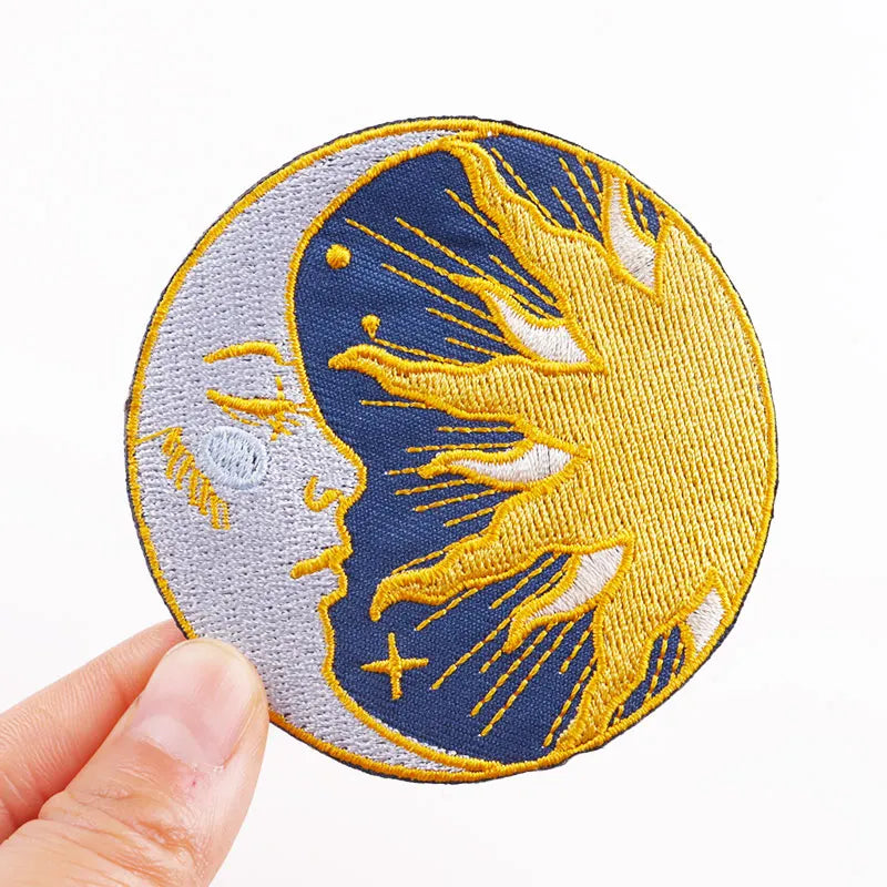 Embroidered patch with a design of a face on a half moon held by a hand against a white background