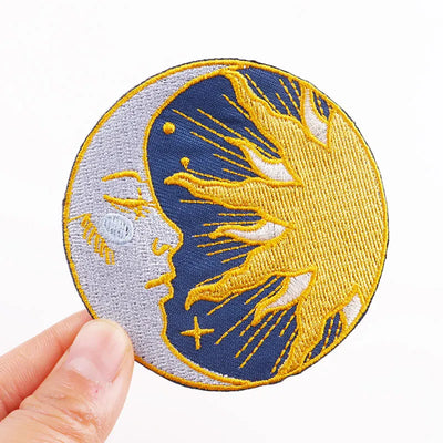 Embroidered patch with a design of a face on a half moon held by a hand against a white background