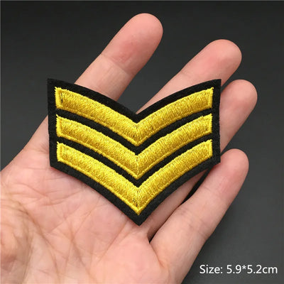 Yellow and black embroidered patch with three chevrons held in a hand against a dark background