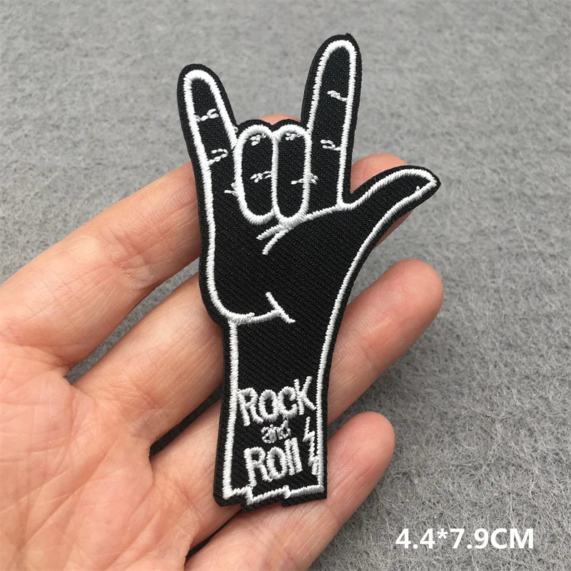 Hand holding a black and white 'Rock and Roll' hand gesture patch on a gray background