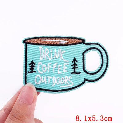 Embroidered patch of a coffee cup with 'Drink Coffee Outdoors' text on a light blue background.