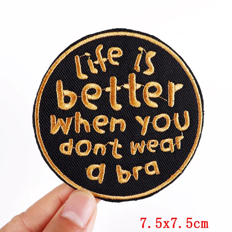Round patch with embroidered text 'Life is better when you don't wear a bra' held by a hand.