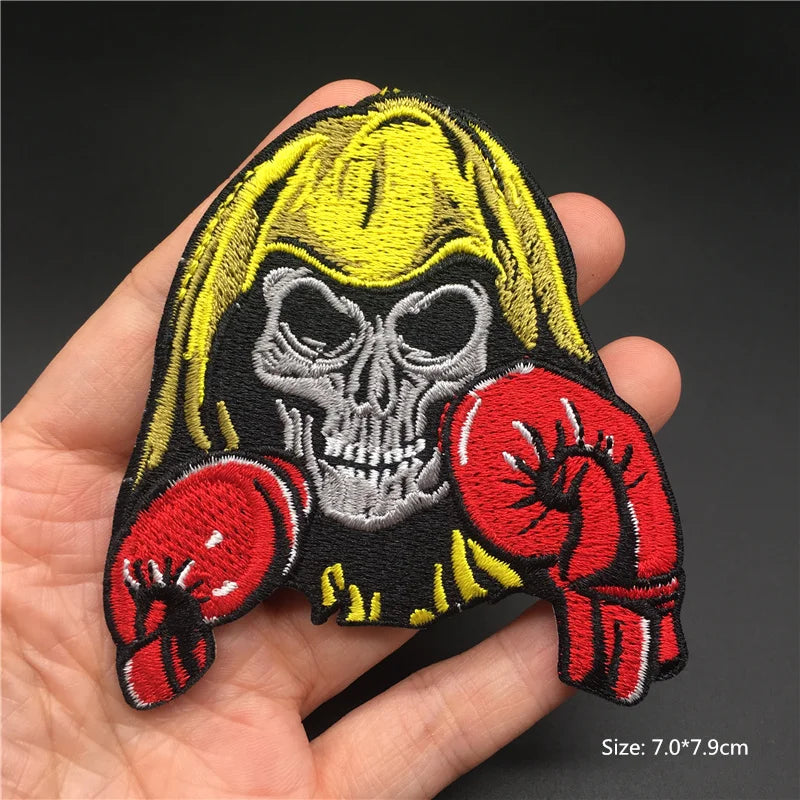 Skull with yellow hair and red boxing gloves patch held in a hand against a dark background