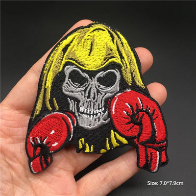 Skull with yellow hair and red boxing gloves patch held in a hand against a dark background