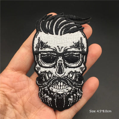 Black and white embroidered patch of a skull with hair held in a hand against a dark background
