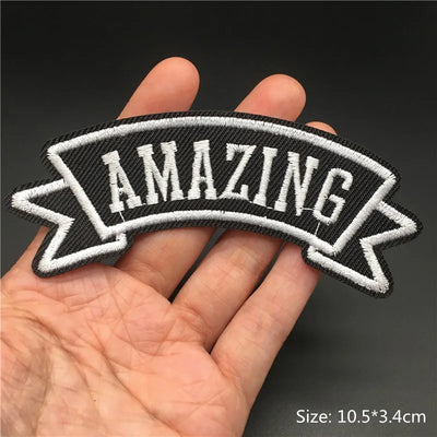 Black and white 'AMAZING' patch held in a hand with a dark background