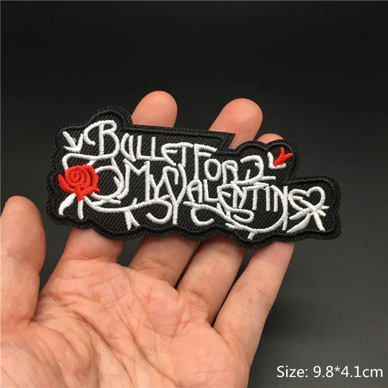 Embroidered patch with text and red rose held in a hand against a dark background