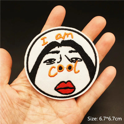 Patch with face design and 'I am cool' text held in a hand against a dark background
