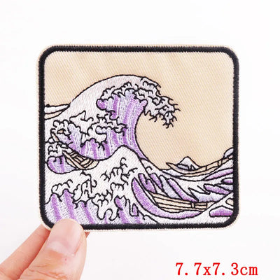 Embroidered patch with wave design held by a hand, on a beige background.