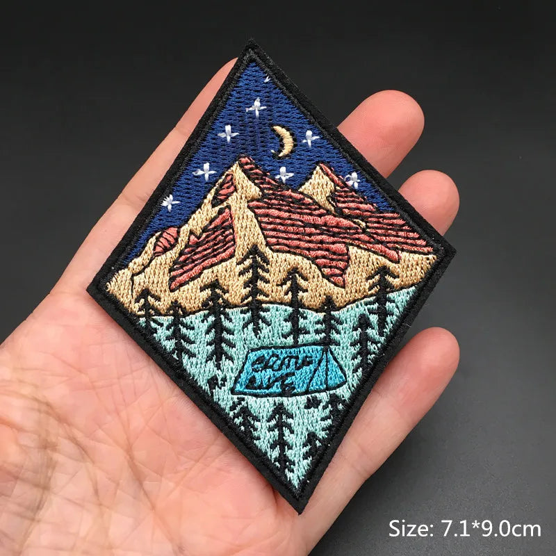 Embroidered patch of mountains and trees held in a hand with a dark background