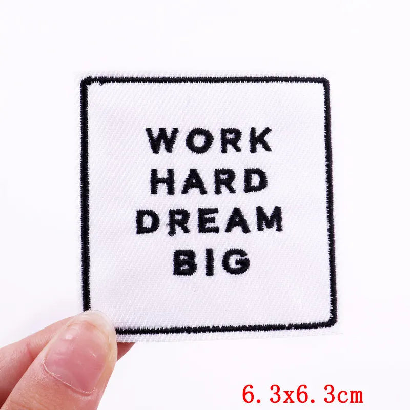 Embroidered patch with 'Work Hard Dream Big' text held by a hand on a white background.