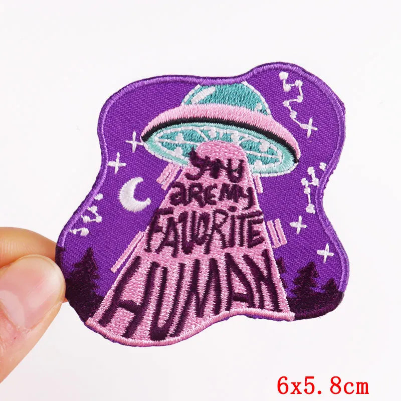 Embroidered patch with a mushroom design and text on a purple background, held by a hand.